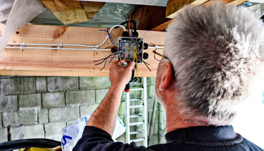 Elektryk kończy instalację elektryczną w garażu, łącząc przewody w puszce.