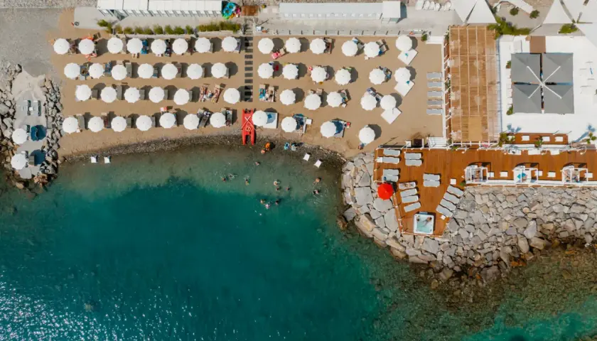 Vue aérienne d'une plage de Diano Marina avec des parasols blancs, des chaises longues, des baigneurs dans la mer turquoise et un jacuzzi sur la jetée.