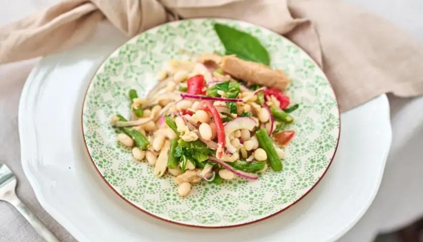 Ein bunter Thunfisch-Bohnen-Salat, italienisch inspiriert, mit grünen Bohnen, roten Zwiebeln und Tomaten auf einem Teller mit grünem Muster.