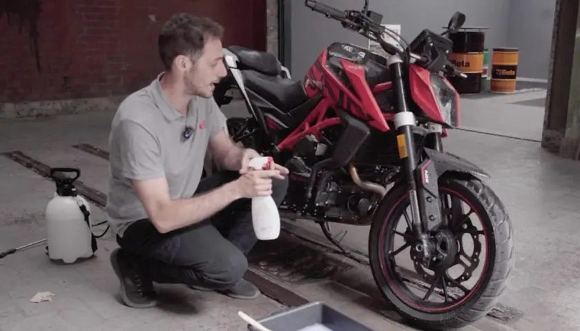 Uomo con spray e secchio di schiuma, pronto a usare prodotti casalinghi per lavare moto.