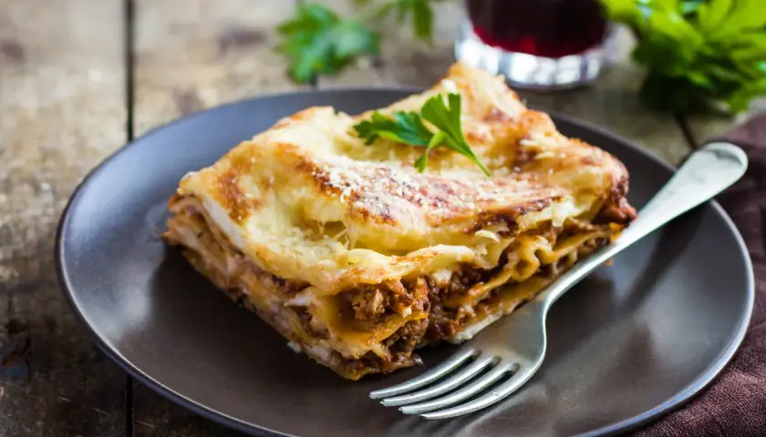 Pyszna lasagne z mielonym mięsem, idealna odpowiedź na pytanie: jakie mięso do lasagne. Podana na talerzu z widelcem.
