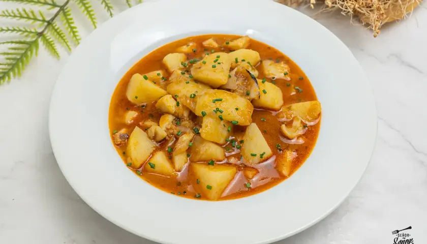 Plato de patatas con sepia, un guiso casero que evoca las patatas con sepia de la abuela, con trozos de patata y sepia en una salsa rojiza.