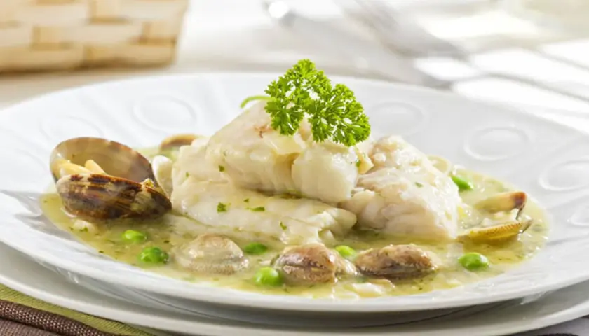 Merluza en salsa verde con almejas y guisantes, decorada con perejil fresco. Un plato marinero delicioso.