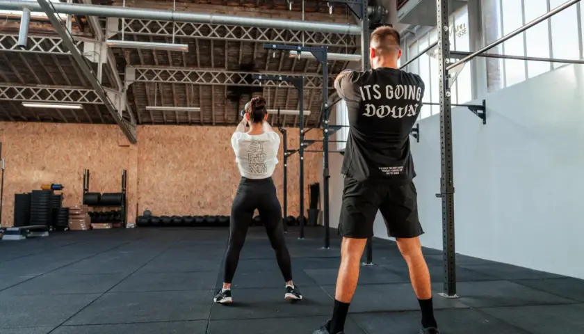 Para pozuje na siłowni. Ona wykonuje ćwiczenie z kettlebell, on stoi z tyłu. To właśnie crossfit co to za trening!