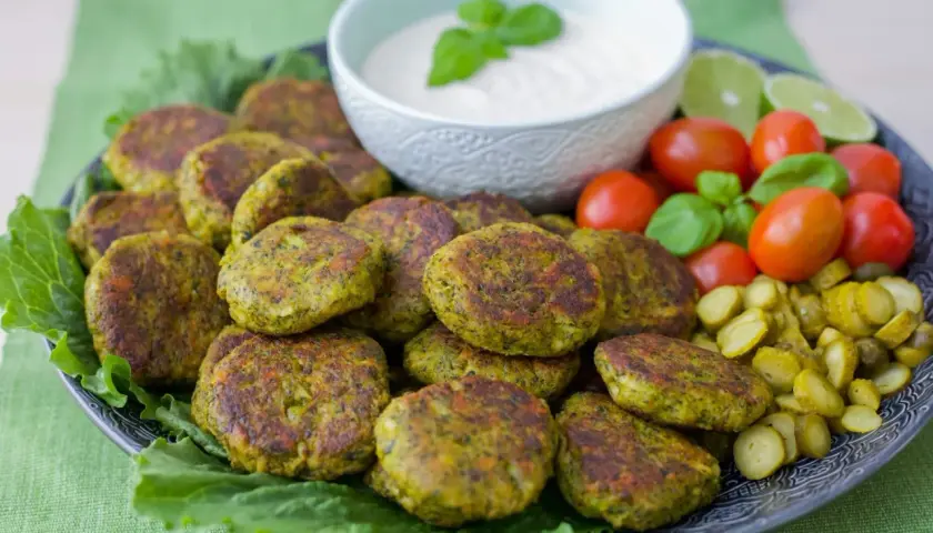 En tallrik med gyllene vegetariska biffar, serverade med en krämig dipp, körsbärstomater, gurkskivor och limeklyftor.