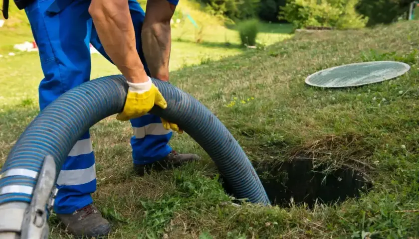 Pracownik w żółtych rękawicach obsługuje wąż do wywozu szamba. Sprawdź nasz wywóz szamba cennik i zadbaj o czystość.
