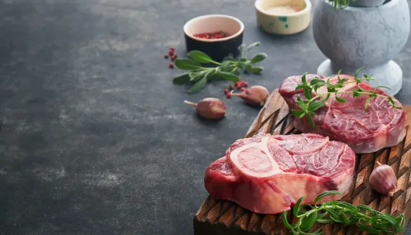 Deux grosses pièces de viande au barbecue, prêtes à être grillées, avec des herbes fraîches et de l'ail.