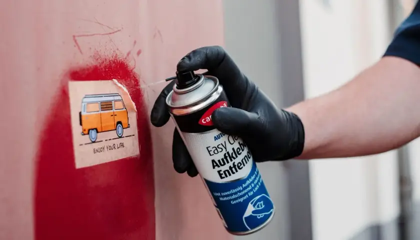 Mit einem Spray werden klebereste von kunststoffrahmen entfernt. Ein Aufkleber mit einem Camper wird gerade bearbeitet.