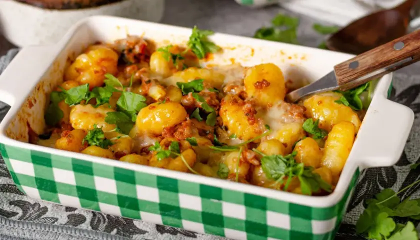 Zapiekane gnocchi z pomidorami i mozzarellą, posypane świeżą natką pietruszki, w zielono-białej kratce. Pyszne danie gotowe do podania.
