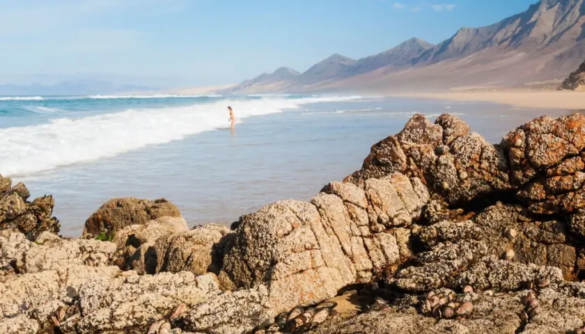 Una persona disfruta de las playas nudistas de Cantabria, con olas rompiendo en la costa y montañas al fondo.