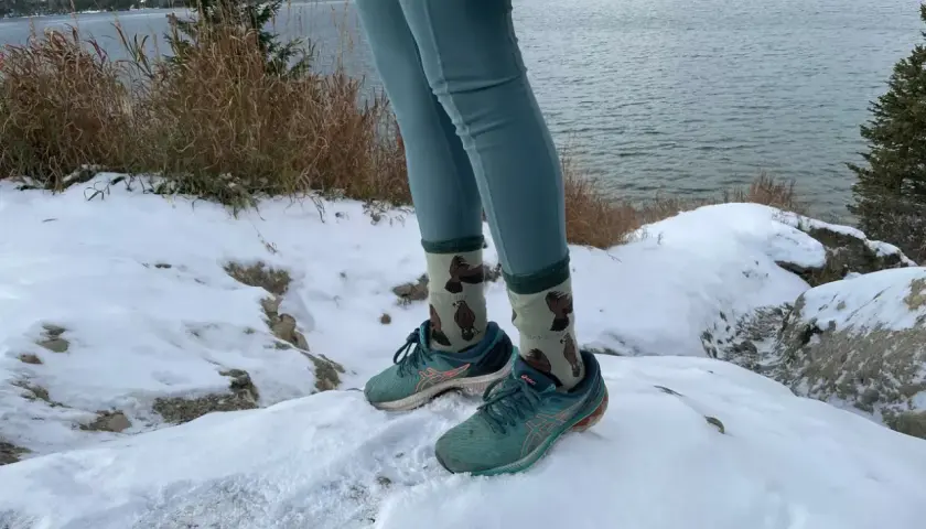 Wygodne leginsy w góry i buty do biegania na śniegu. W tle jezioro i ośnieżone szczyty.