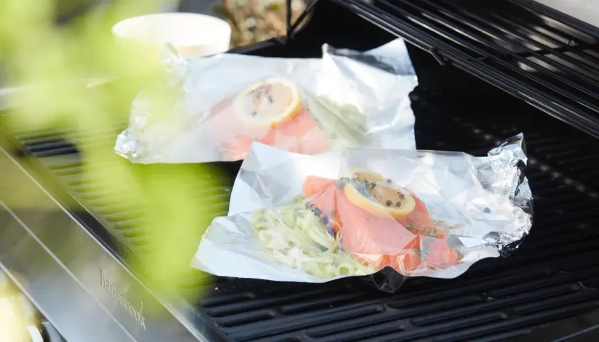 Deux papillotes de saumon en préparation sur un barbecue, prêtes à être cuites.