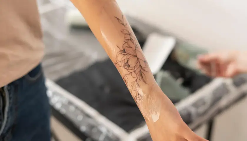 Un bras orné d'un tatouage floral délicat, la peau légèrement humide, comme si elle commençait à peler après la séance.