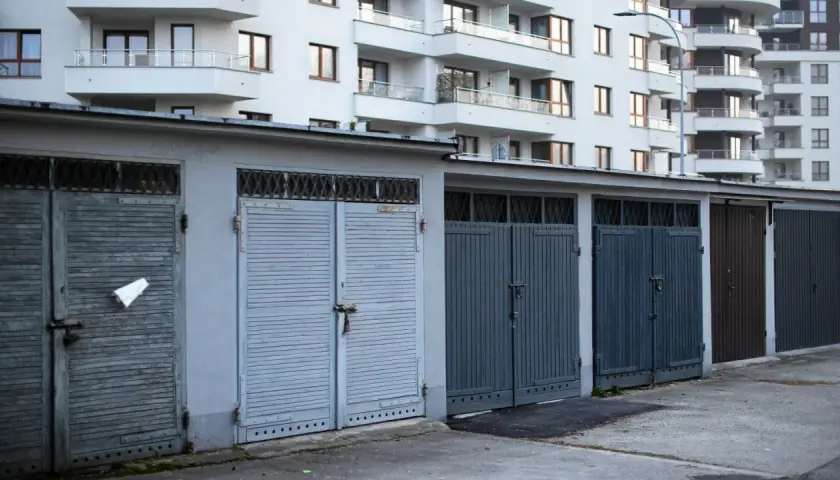 Rząd garaży wolnostojących zamykanych na kłódki, na tle nowoczesnego bloku mieszkalnego. Zastanawiasz się, ile kosztuje garaż wolnostojący?