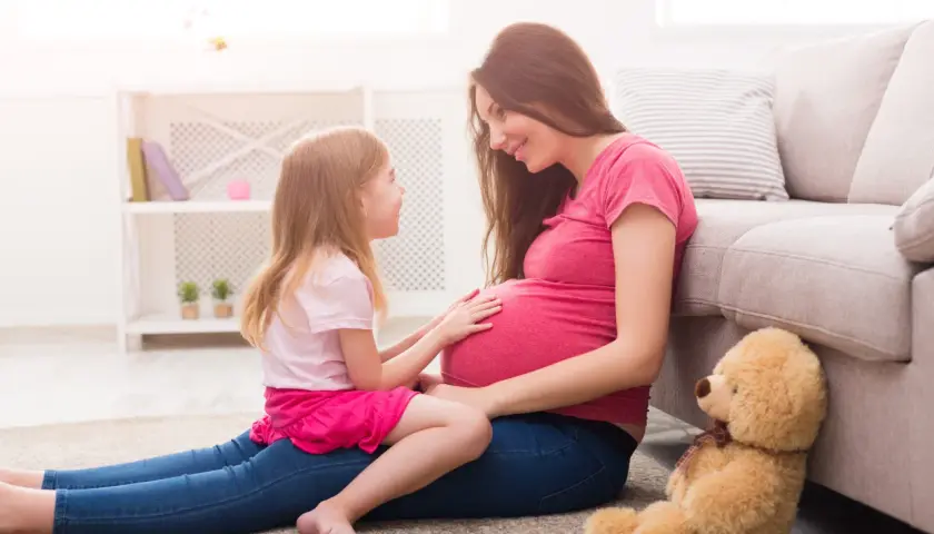 Córka z czułością dotyka brzucha mamy, która wyjaśnia jej, jak wytłumaczyć 10 latkowi skąd się biorą dzieci. Miś czeka na nowego członka rodziny.