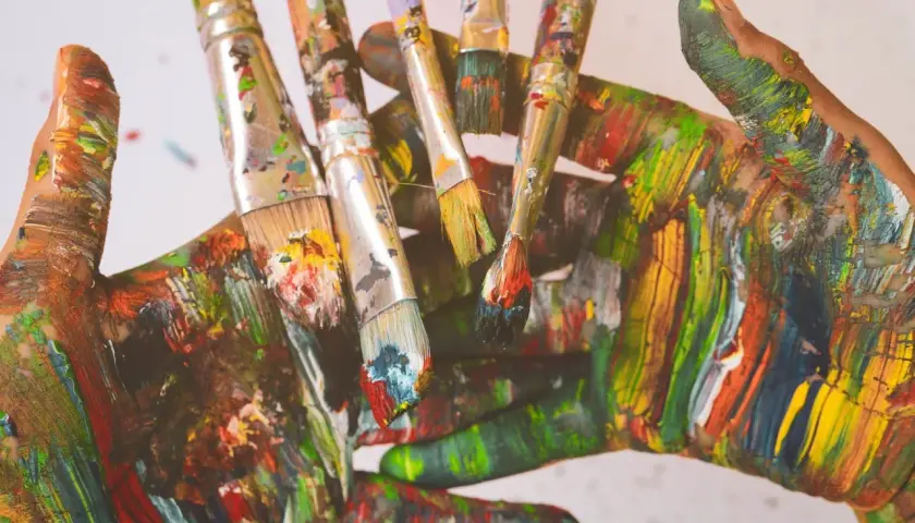 Bunte Hände und Pinsel, die zeigen, wie man grau mischt, indem man alle Farben übereinanderlegt.