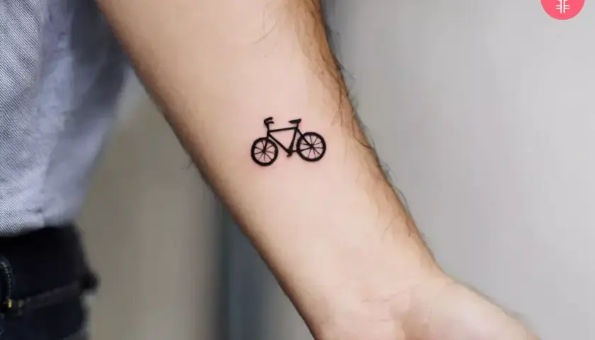 Minimalistyczny tatuaż rower szosowy na przedramieniu. Symbol wolności i pasji do podróży.