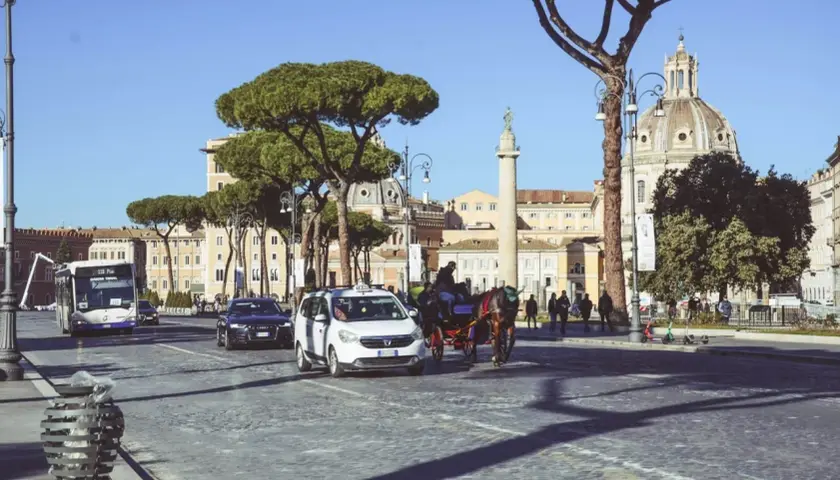 Carrozze, taxi e bus sfrecciano su un lastricato romano, con la cupola del Vaticano in lontananza. La distanza stazione Termini Vaticano è breve.
