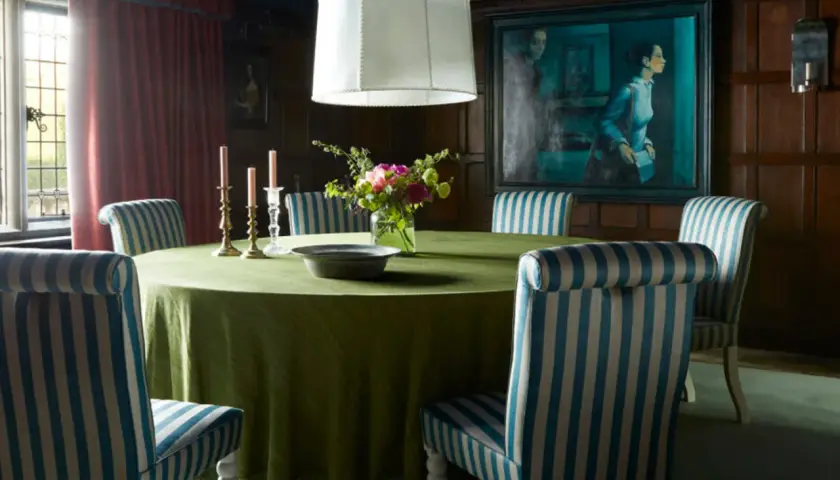 A dining room with a round green table, striped chairs, and a large painting. The table styles are classic and elegant.