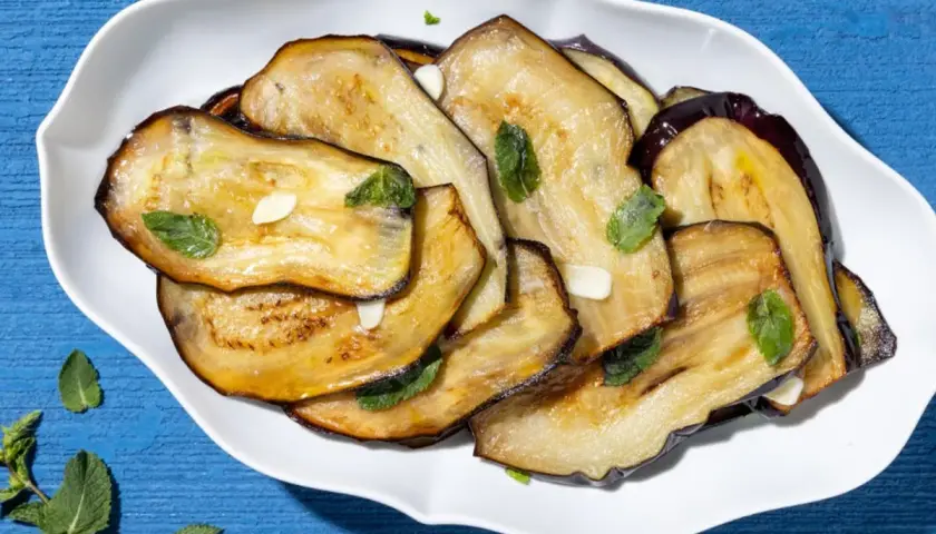 Fette di melanzane grigliate, guarnite con menta fresca e aglio. Un contorno di verdure semplice e gustoso.