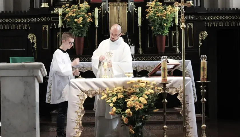 Ksiądz i ministrant podczas mszy świętej przy ołtarzu ozdobionym kwiatami.