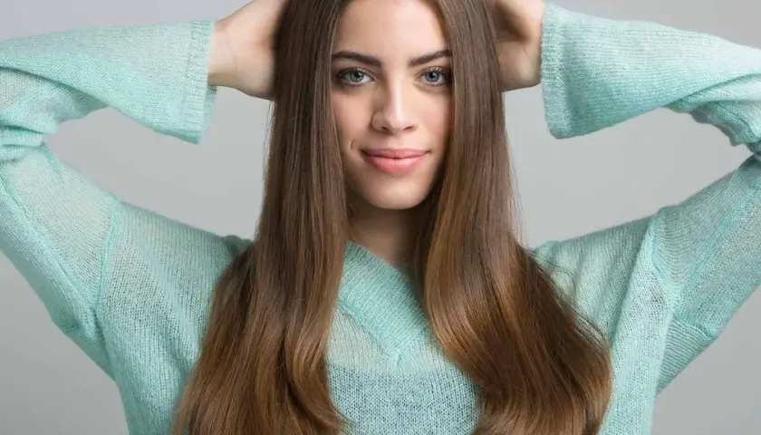 Joven sonríe con las manos en la cabeza, su cabello castaño cae sobre sus hombros. Apenas se notan las primeras canas, un toque de madurez.