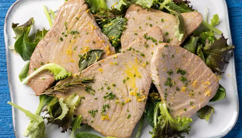 Fette di tonno al forno, profumate al limone e erbe aromatiche, servite su un letto di insalata fresca.