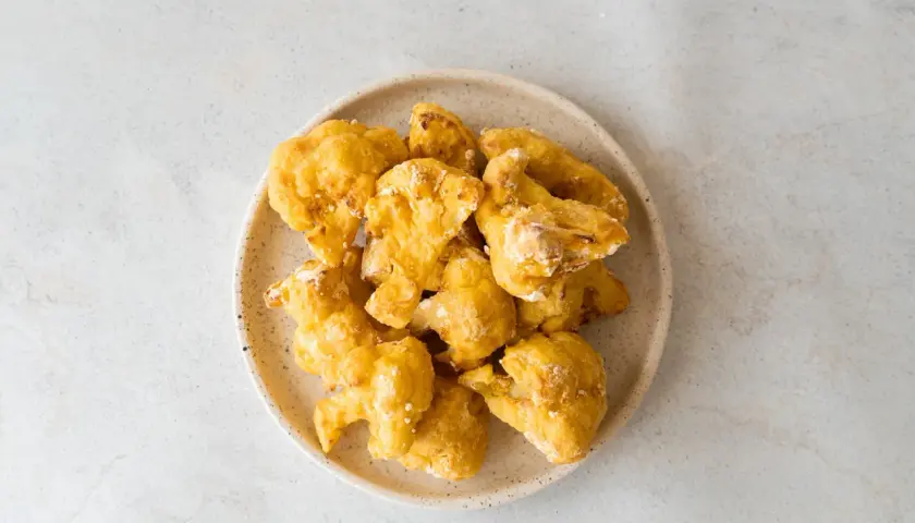 Alitas de coliflor doradas y crujientes en un plato, listas para disfrutar.