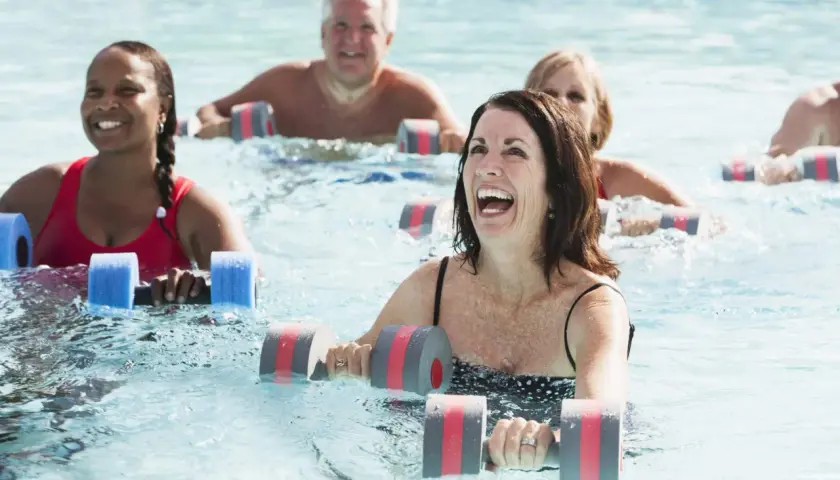 Personas sonriendo y haciendo aqua gym en una piscina con pesas flotantes.