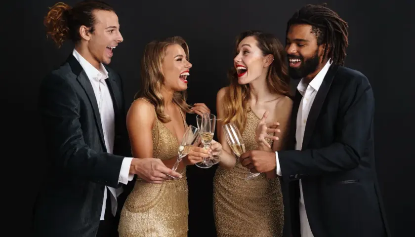 Pareja brindando en una fiesta, cumpliendo el dress code fiesta con trajes elegantes y vestidos dorados.