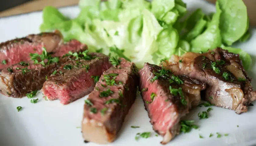 Tranches de steak black angus saignant, garnies de persil frais, servies avec de la laitue croquante sur une assiette blanche.