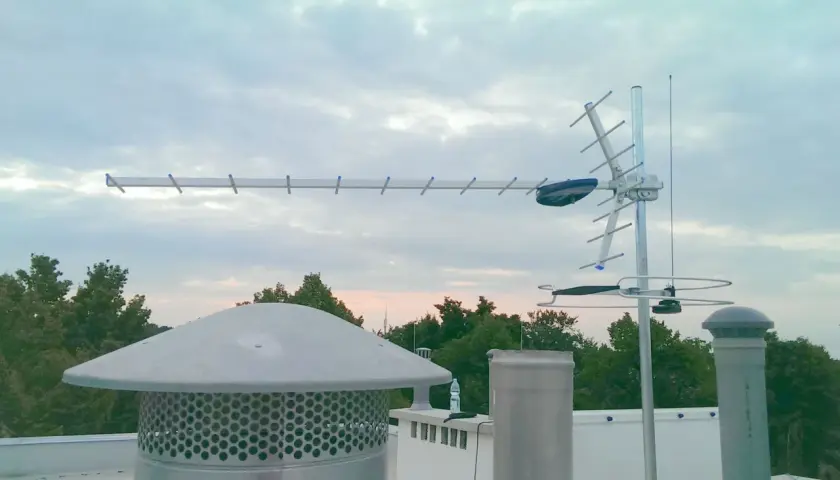 Antena telewizji naziemnej na dachu, na tle nieba i drzew.