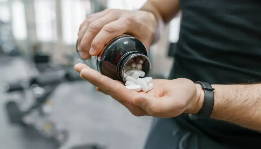 Mann schüttet weiße Pillen aus einer Flasche in seine Hand. Möglicherweise zur Unterstützung der Yohimbin Wirkung im Fitnessstudio.