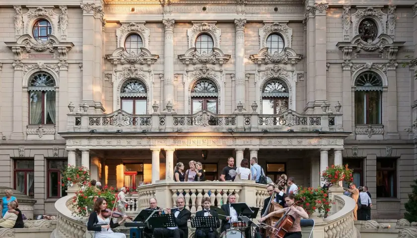 Koncert kameralny przed pałacem poznańskiego w Łodzi. Orkiestra gra na tarasie, a widzowie słuchają na schodach.