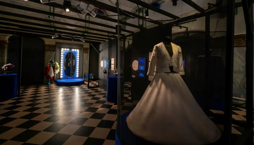 En vit dansklänning visas upp i en monter på Dansmuseet Stockholm. Golvet har ett schackrutigt mönster.