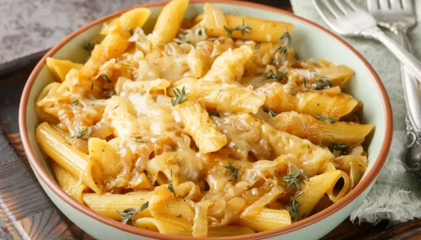 Makaron penne z karmelizowaną cebulą i roztopionym serem, ozdobiony tymiankiem.
