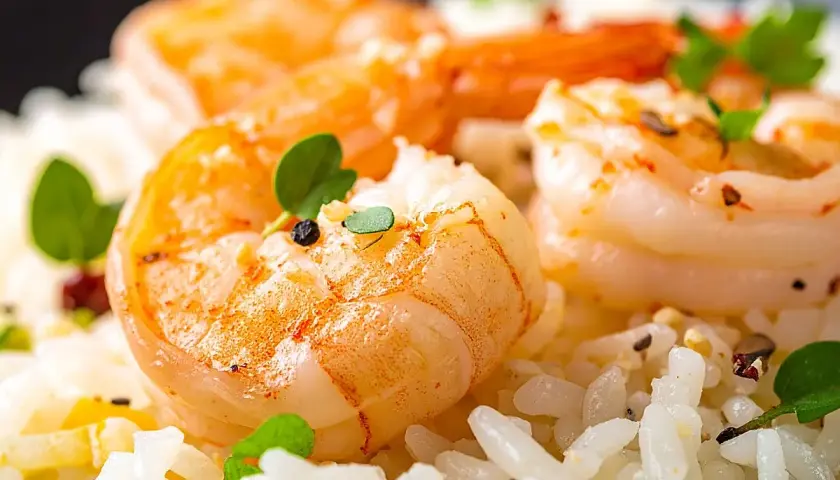 Delicioso arroz con gambas y verduras, adornado con hierbas frescas y granos de pimienta.