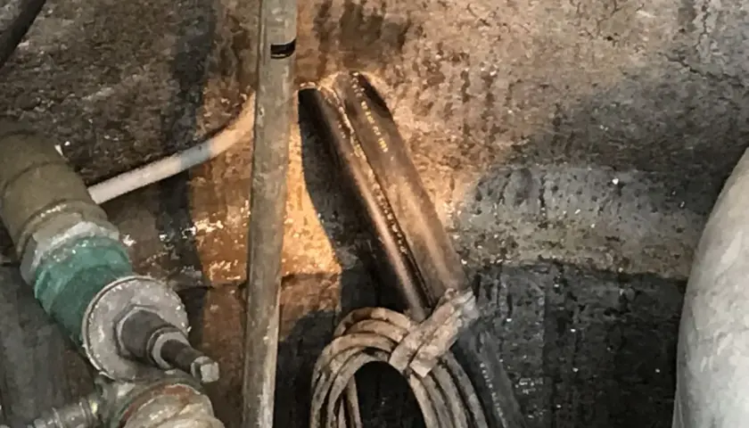 Rohrleitungen und Kabel in einem feuchten Bereich, der auf eine notwendige **Brunnenabdichtung** hindeutet.
