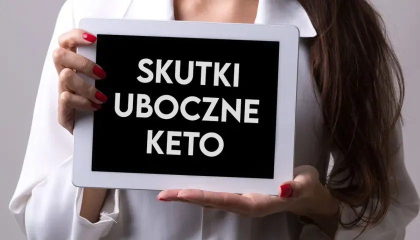 Kobieta trzyma tablet z napisem "SKUTKI UBOCZNE KETO". Zastanawiasz się nad dietą keto? Poznaj potencjalne skutki uboczne.