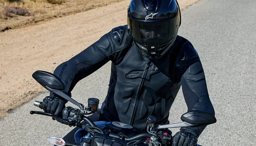 Motocyklista w kasku i czarnej kurtce Alpinestars jedzie po pustynnej drodze.