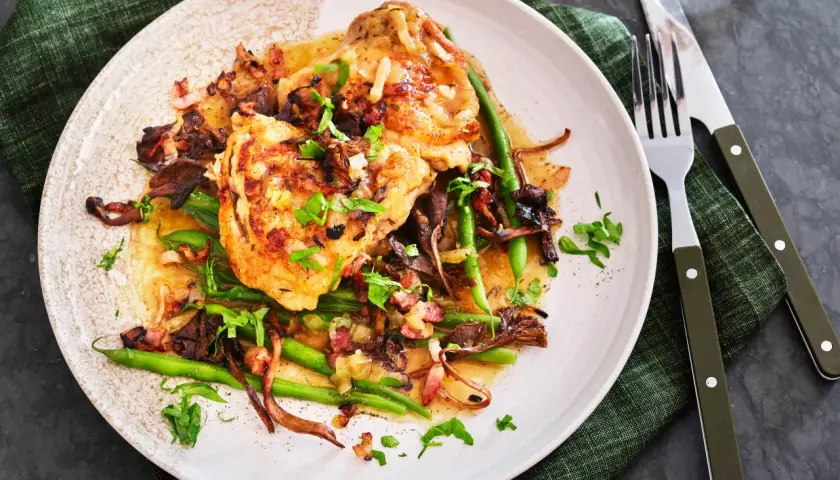 En tallrik med kyckling i vitvinssås, svamp, haricots verts och bacon. En utsökt coq au vin blanc.