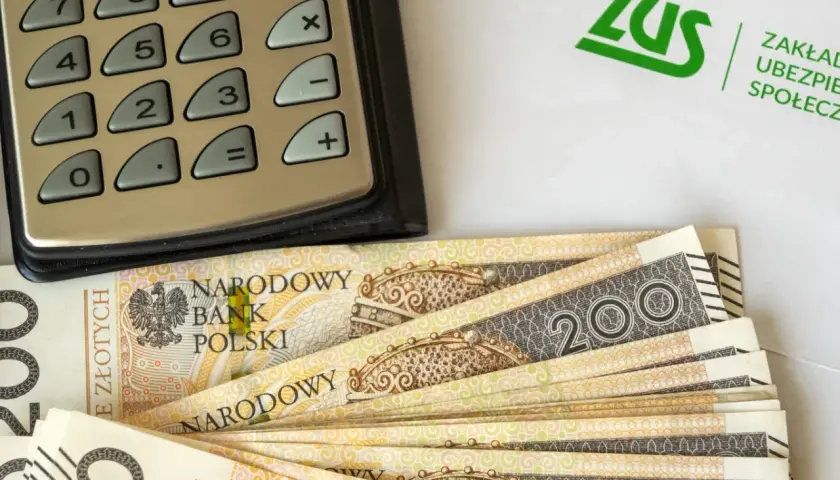 Kalkulator, banknoty 200 zł i logo ZUS. Obliczenia dotyczące tego, ile wynosi dodatek do emerytury za warunki szkodliwe.