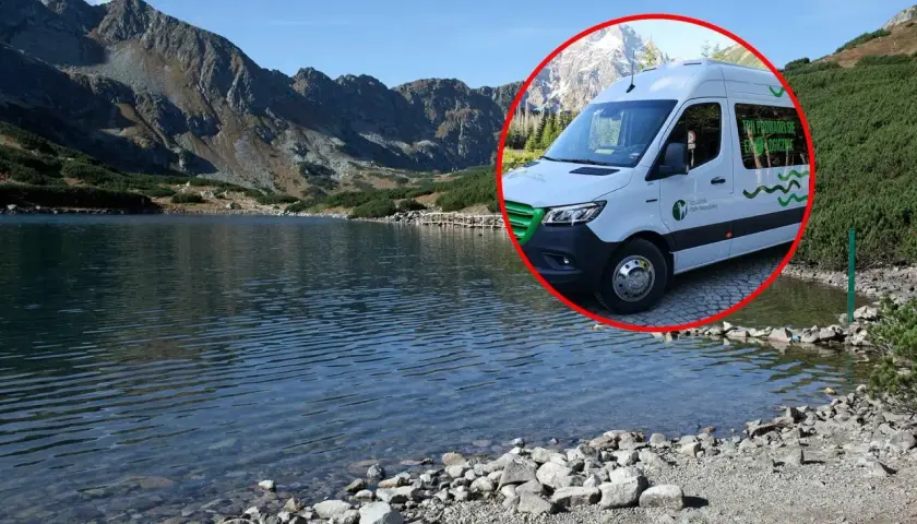 Biały bus do Morskiego Oka stoi przy tafli jeziora, w tle góry.