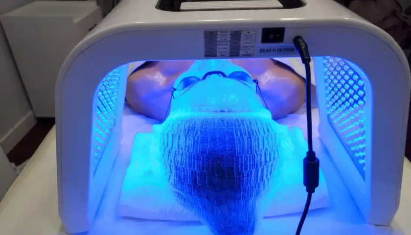 Kobieta poddana zabiegowi fototerapii twarzy w salonie kosmetycznym. Urządzenie OMEGA LIGHT emituje niebieskie światło.