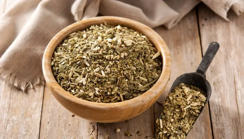 Suszone liście yerba mate w drewnianej misce i szufelce. Choć yerba mate ma wiele zalet, warto pamiętać o jej negatywnych właściwościach, np. o zawartości kofeiny.