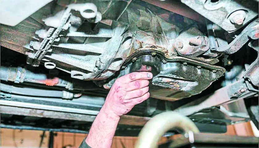 Mano revisa el cárter de un coche, mostrando signos de perdida de aceite.