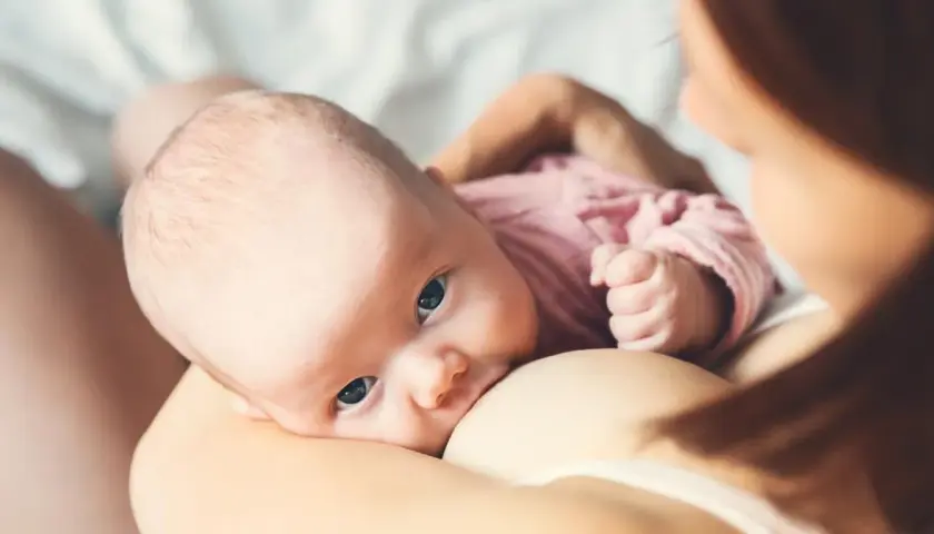 Niemowlę karmione piersią, z uwagą wpatrujące się w obiektyw. To piękny okres macierzyństwa.