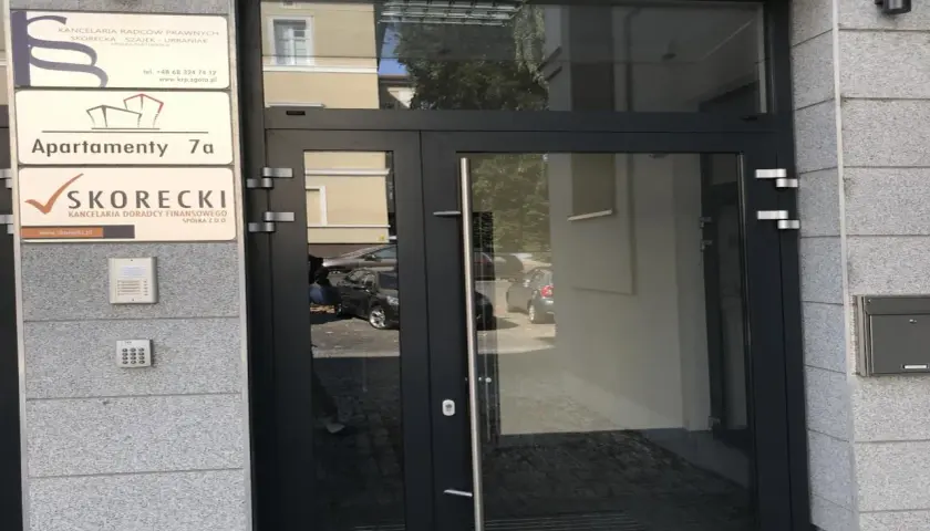 Drzwi wejściowe do budynku z tabliczkami informacyjnymi, w tym "SKORECKI KANCELARIA DORADCY FINANSOWEGO".