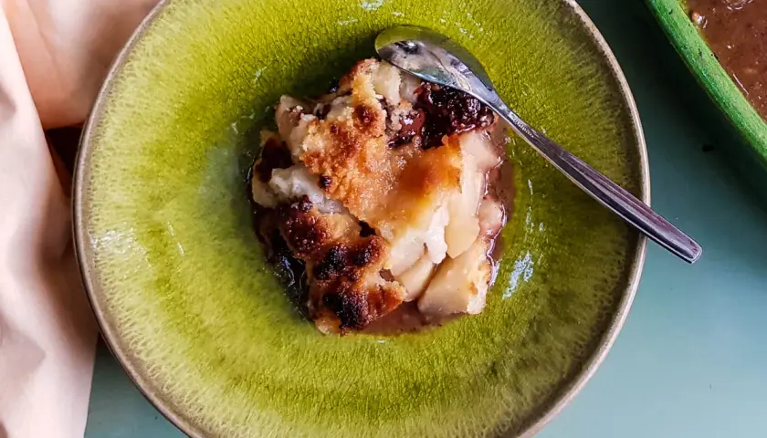 Un délicieux crumble poire chocolat, doré et croustillant, servi dans une assiette verte avec une cuillère.