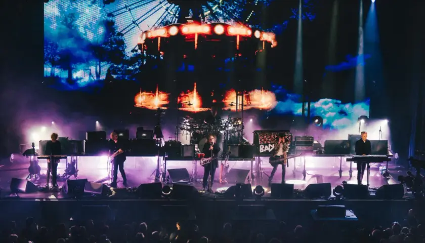 The Cure Polska na żywo. Zespół gra na scenie, w tle wielki ekran z karuzelą.